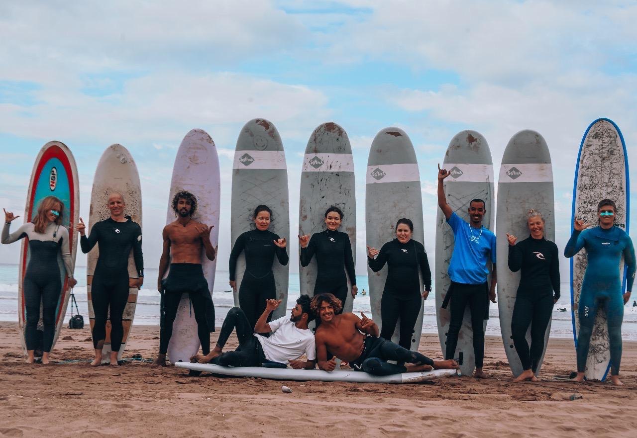L'équipe de Harmony Surf Lodge sur la plage avec les planches, l'océan derrière